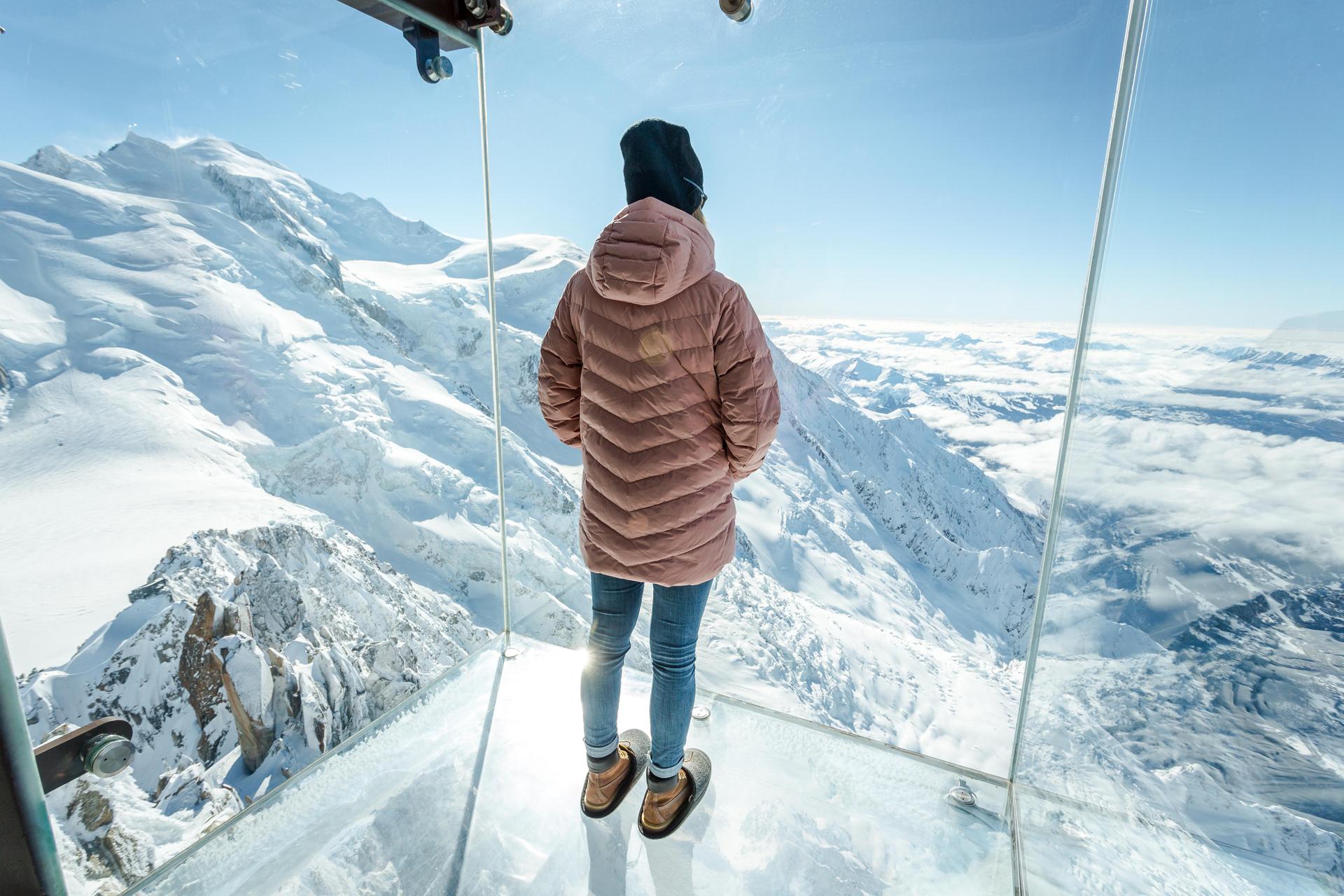 Person standing in a glass room over the mountains surrounding